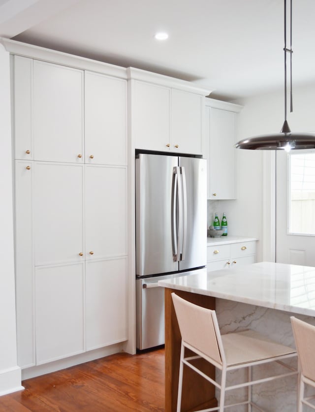 kitchen featuring freestanding refrigerator, white cabinets, decorative light fixtures, and wood finished floors