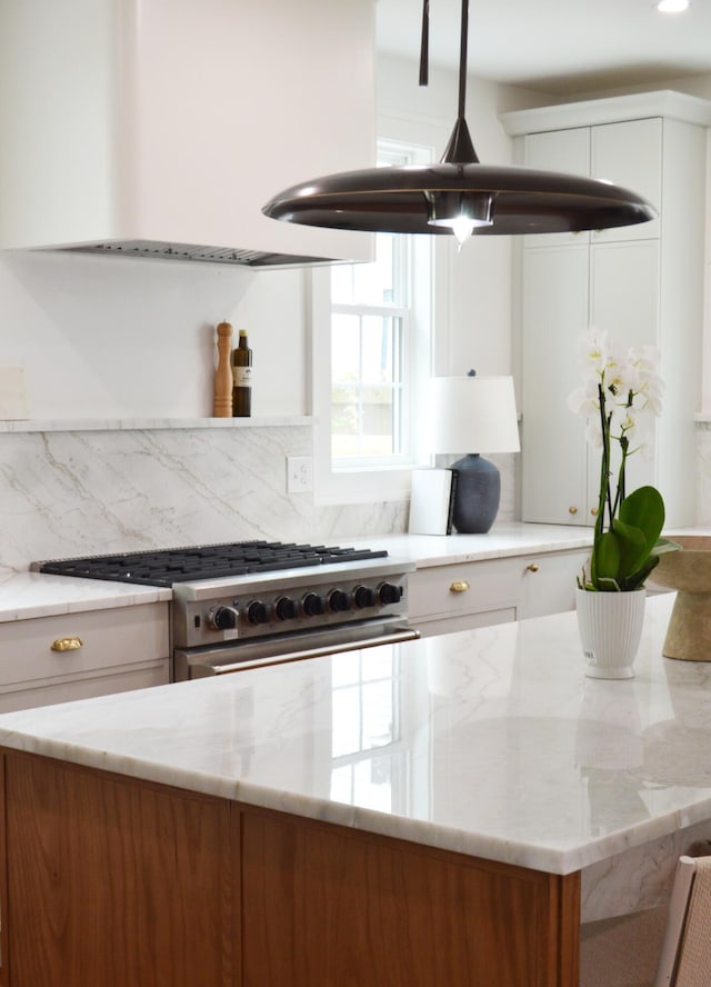kitchen with tasteful backsplash, light stone countertops, white cabinets, and stainless steel range