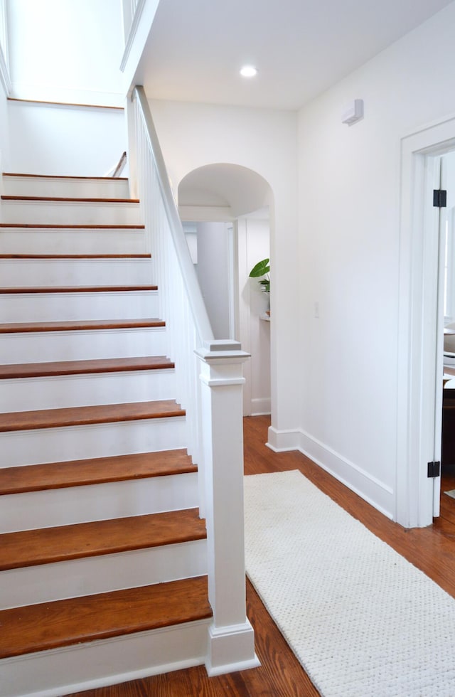 staircase featuring recessed lighting, arched walkways, baseboards, and wood finished floors