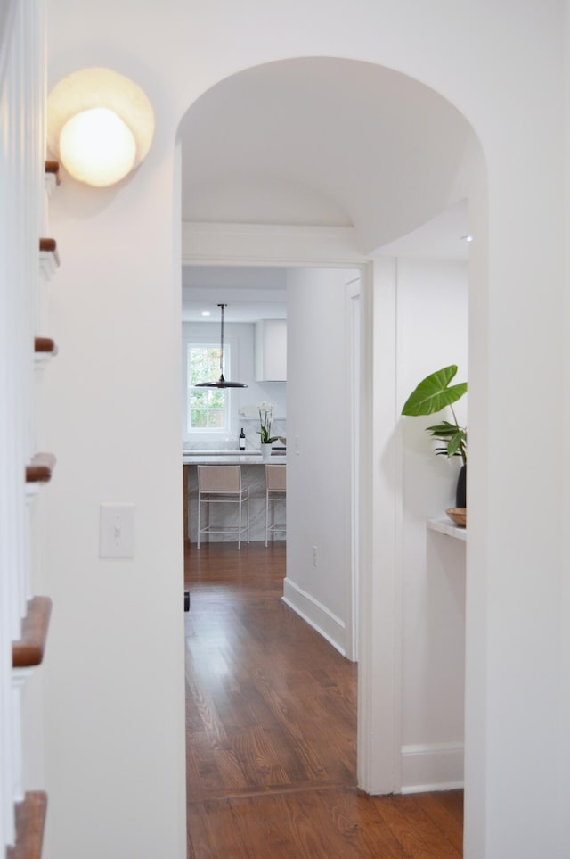 hallway featuring arched walkways, dark wood-style flooring, and baseboards