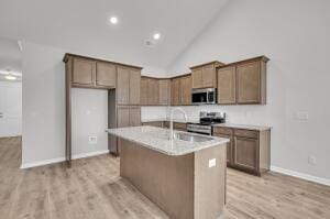 kitchen with a sink, light wood-type flooring, appliances with stainless steel finishes, and a kitchen island with sink