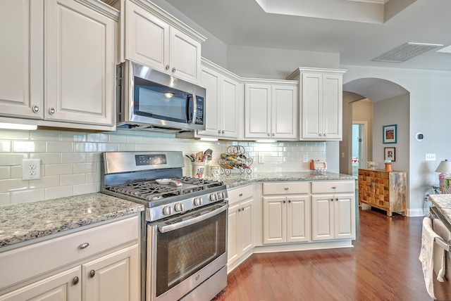 kitchen with light wood-type flooring, arched walkways, appliances with stainless steel finishes, white cabinetry, and visible vents