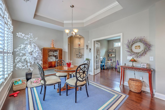 dining room with a tray ceiling, baseboards, built in shelves, wood finished floors, and ornamental molding