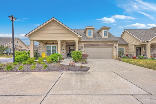 craftsman-style home featuring a shingled roof, driveway, covered porch, stone siding, and a garage