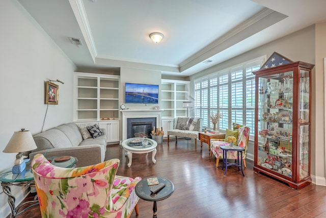 living area featuring a tray ceiling, visible vents, ornamental molding, a glass covered fireplace, and hardwood / wood-style flooring