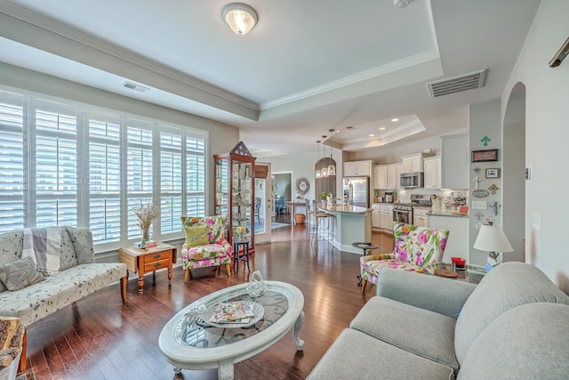 living area featuring arched walkways, visible vents, ornamental molding, and a tray ceiling
