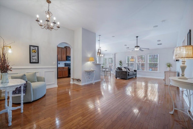 living room with ceiling fan with notable chandelier, vaulted ceiling, and light hardwood / wood-style floors