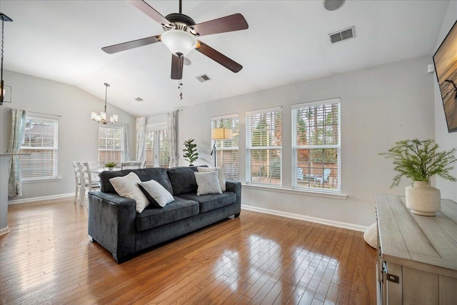 living room with vaulted ceiling, ceiling fan with notable chandelier, light hardwood / wood-style floors, and a wealth of natural light