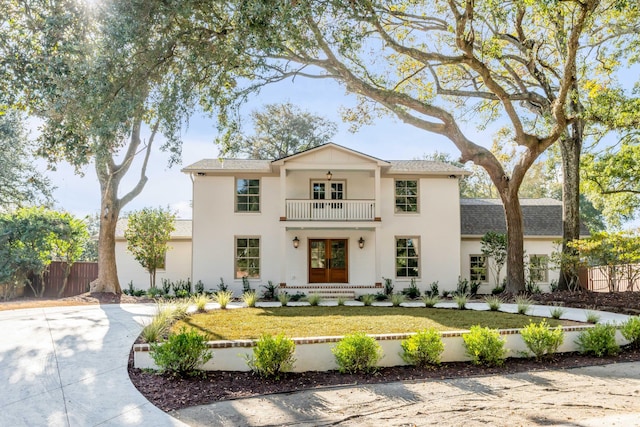 view of front of property featuring fence, stucco siding, a front yard, a balcony, and french doors