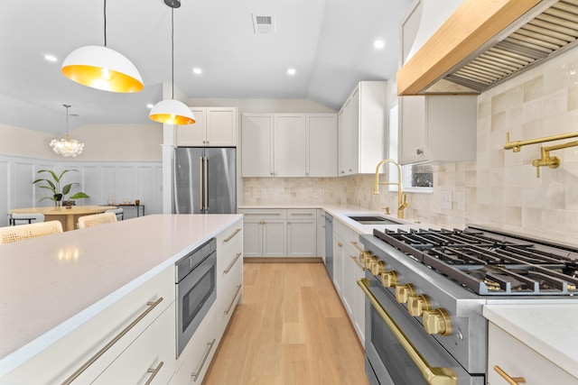 kitchen with premium range hood, white cabinetry, high end appliances, and sink