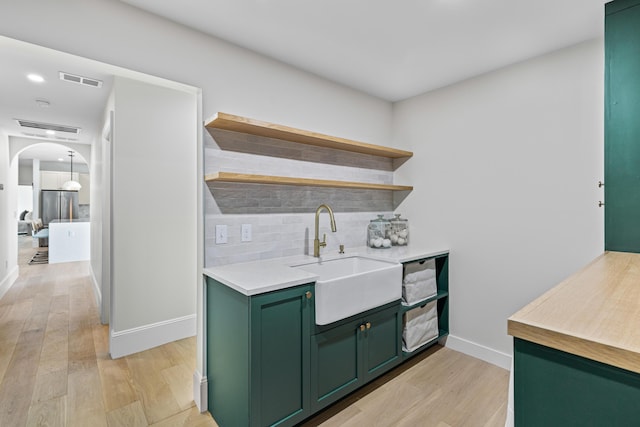 bar featuring backsplash, green cabinets, sink, and light hardwood / wood-style flooring