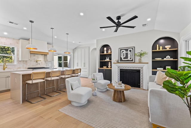 living room featuring built in shelves, lofted ceiling, light hardwood / wood-style flooring, and a healthy amount of sunlight