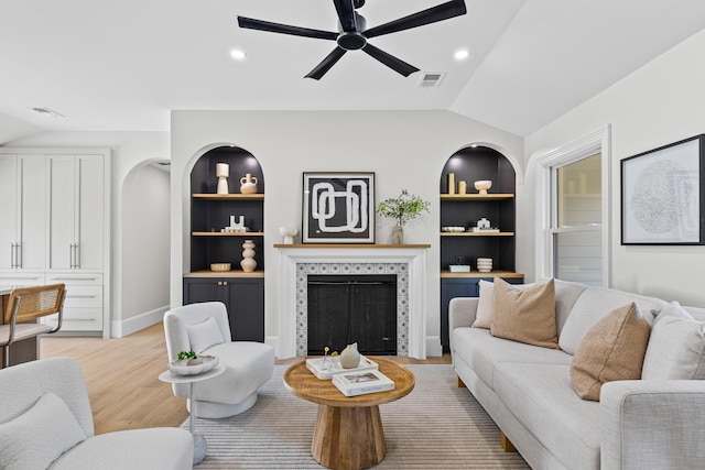 living room with ceiling fan, a tile fireplace, light hardwood / wood-style flooring, built in features, and lofted ceiling