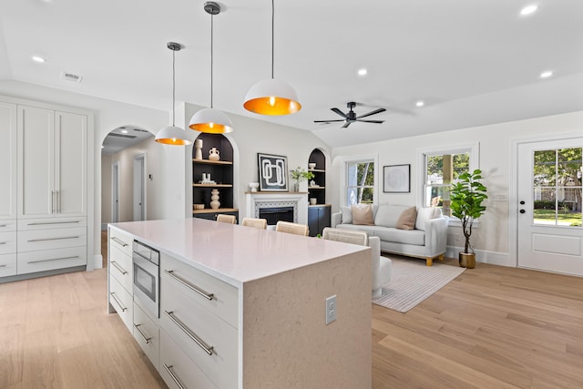 kitchen with ceiling fan, decorative light fixtures, a tiled fireplace, white cabinets, and light wood-type flooring