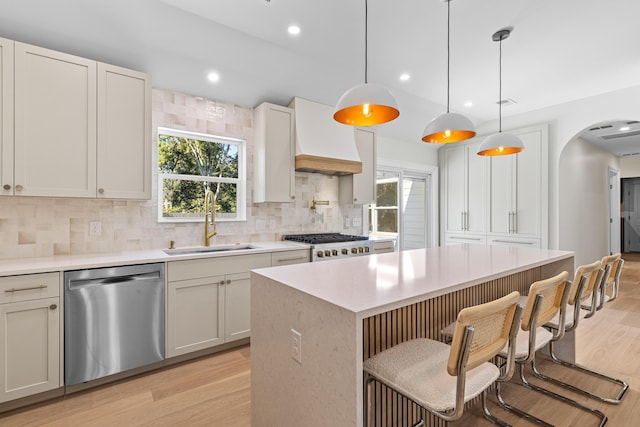 kitchen with sink, hanging light fixtures, premium range hood, appliances with stainless steel finishes, and light wood-type flooring