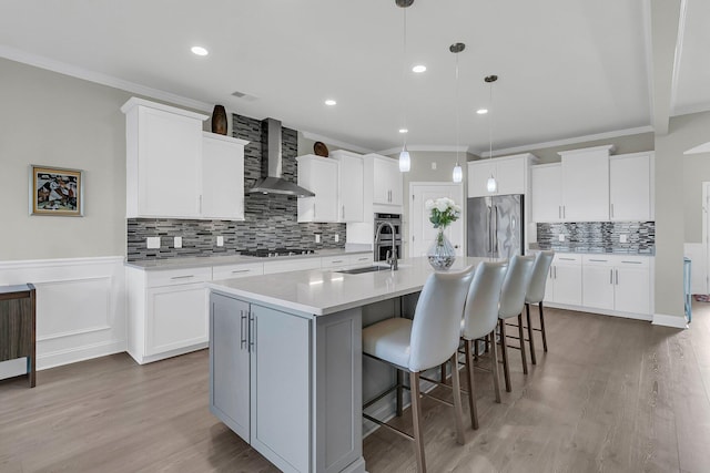 kitchen featuring white cabinetry, a kitchen island with sink, stainless steel appliances, decorative light fixtures, and wall chimney exhaust hood