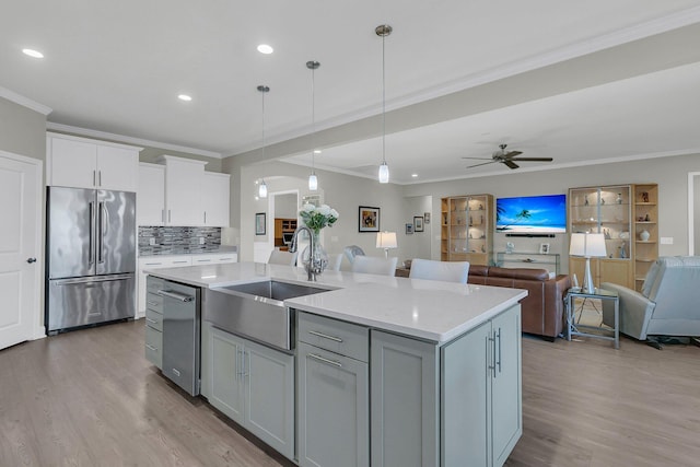 kitchen featuring a center island with sink, stainless steel appliances, decorative light fixtures, ornamental molding, and sink