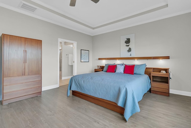 bedroom with a tray ceiling, crown molding, connected bathroom, and hardwood / wood-style flooring