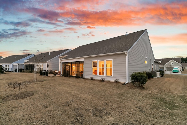 back house at dusk featuring central AC unit and a yard