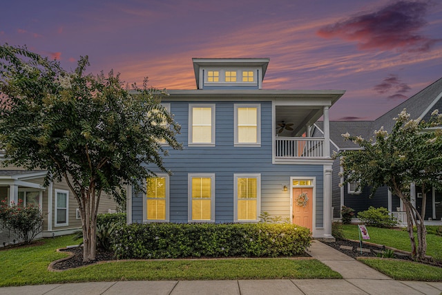 view of front of home featuring a balcony, ceiling fan, and a lawn