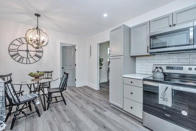 kitchen with backsplash, an inviting chandelier, hanging light fixtures, gray cabinets, and stainless steel appliances