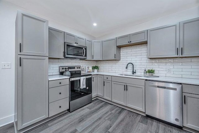 kitchen featuring gray cabinetry, sink, stainless steel appliances, decorative backsplash, and hardwood / wood-style flooring