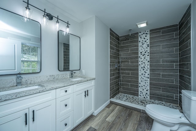 bathroom with wood-type flooring, vanity, toilet, and tiled shower