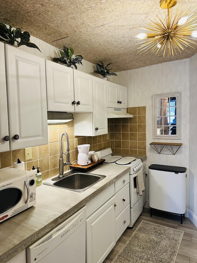 kitchen with a sink, under cabinet range hood, white cabinetry, white appliances, and wallpapered walls