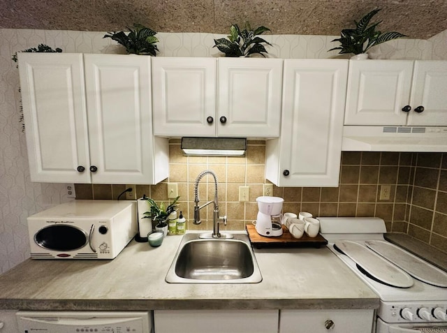 kitchen featuring wallpapered walls, under cabinet range hood, dishwashing machine, white cabinets, and a sink