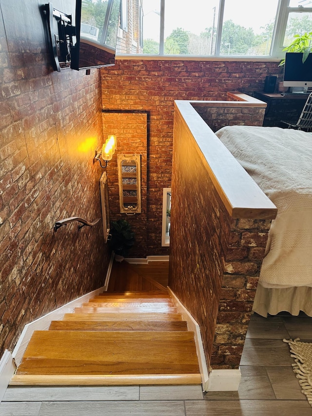 stairs featuring wood finished floors, brick wall, and a towering ceiling