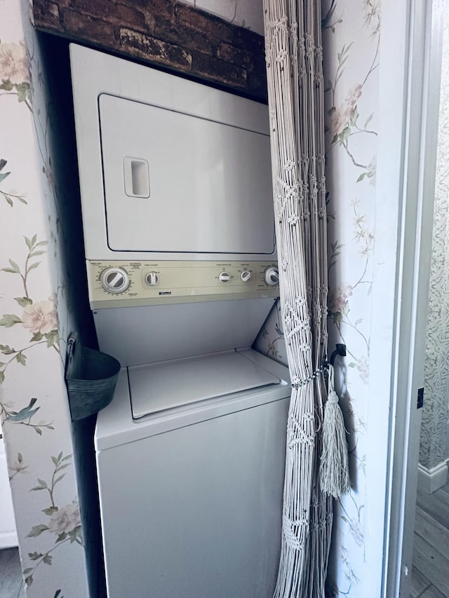 laundry room with stacked washer / dryer, wallpapered walls, and laundry area