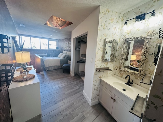 bathroom with a textured ceiling, wood finished floors, wallpapered walls, baseboards, and vanity