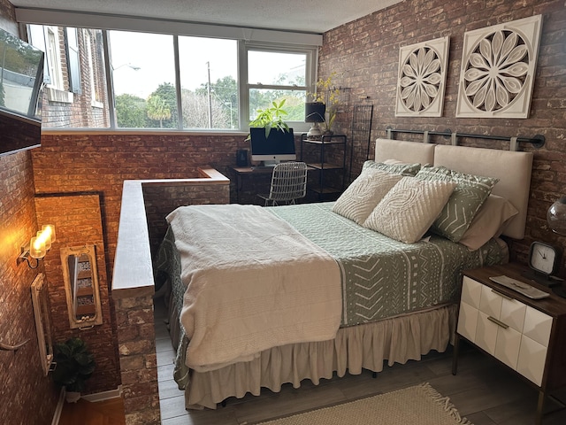 bedroom featuring wood finished floors, brick wall, and a textured ceiling