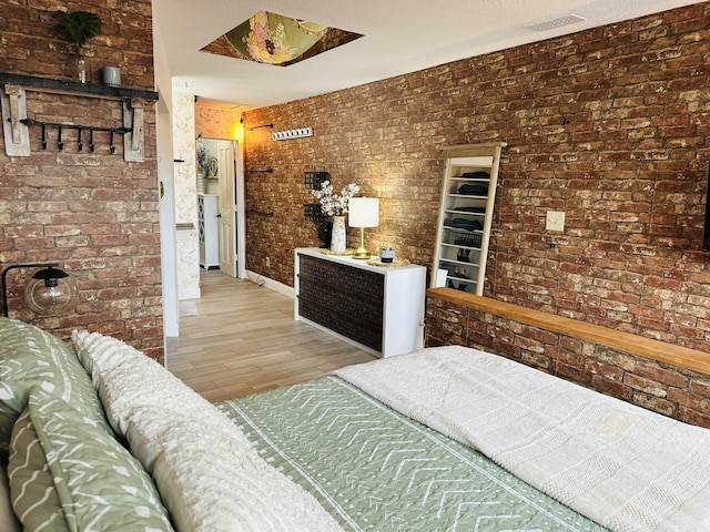 bedroom with light wood finished floors, visible vents, and brick wall