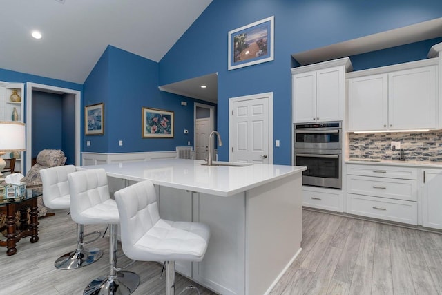 kitchen with a sink, light countertops, double oven, light wood finished floors, and white cabinetry