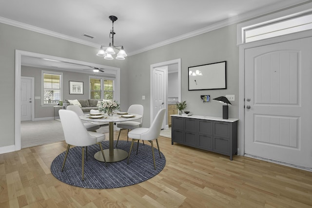 dining space featuring light wood-type flooring, baseboards, visible vents, ceiling fan with notable chandelier, and ornamental molding