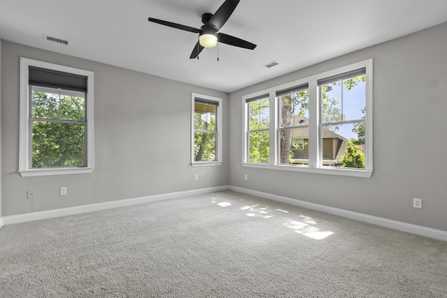 carpeted spare room with plenty of natural light, visible vents, a ceiling fan, and baseboards