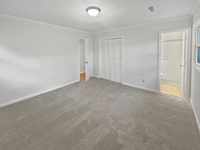 unfurnished bedroom featuring connected bathroom, carpet floors, a textured ceiling, a closet, and ornamental molding