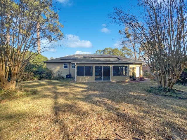 rear view of property with a lawn, a sunroom, and solar panels