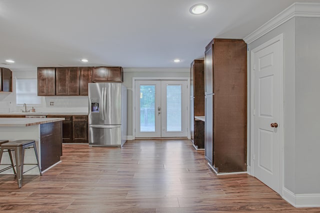 kitchen with backsplash, french doors, light hardwood / wood-style flooring, stainless steel fridge, and a kitchen bar