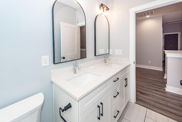 bathroom featuring double vanity, visible vents, toilet, and a sink