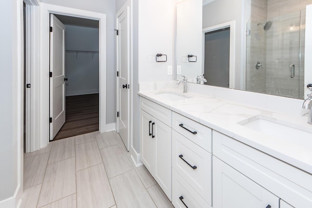 bathroom featuring a spacious closet, a stall shower, double vanity, and a sink