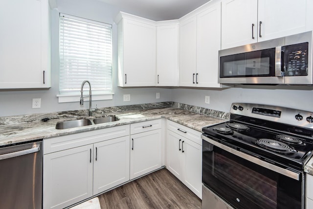 kitchen with a sink, light stone counters, appliances with stainless steel finishes, white cabinets, and dark wood-style flooring