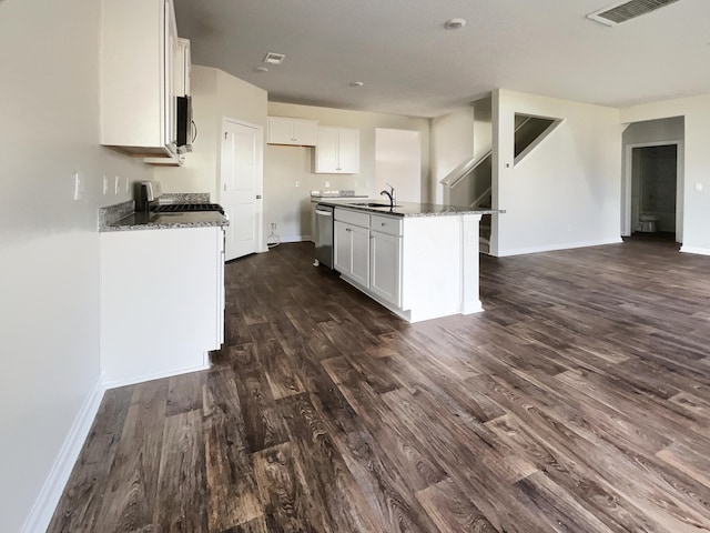 kitchen with a kitchen island with sink, dark stone counters, appliances with stainless steel finishes, dark hardwood / wood-style flooring, and white cabinetry