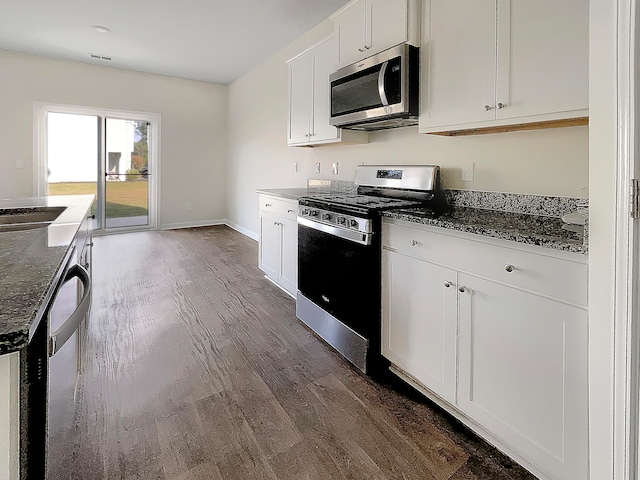 kitchen featuring white cabinets, stainless steel appliances, dark stone counters, and dark wood-type flooring