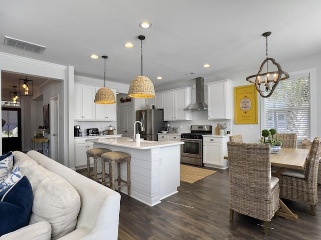 kitchen with light countertops, visible vents, appliances with stainless steel finishes, an island with sink, and wall chimney exhaust hood