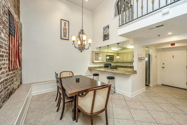 tiled dining space with ornamental molding, sink, brick wall, a high ceiling, and an inviting chandelier