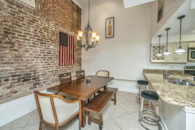 tiled dining area featuring a towering ceiling, a chandelier, brick wall, and sink