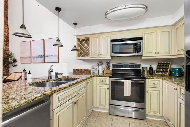 kitchen with appliances with stainless steel finishes, cream cabinetry, sink, and brick wall