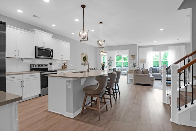 kitchen with a center island with sink, light wood-type flooring, a sink, stainless steel appliances, and recessed lighting